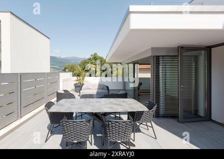 Außenbalkon der Villa modena mit einem kleinen Wohnzimmer bestehend aus einem Sofa, zwei Sesseln und einem Tisch mit Stühlen. Im Hintergrund Schweizer Hügel. Nein Stockfoto