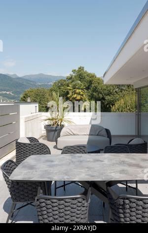 Außenbalkon der Villa modena mit einem kleinen Wohnzimmer bestehend aus einem Sofa, zwei Sesseln und einem Tisch mit Stühlen. Im Hintergrund Schweizer Hügel. Nein Stockfoto