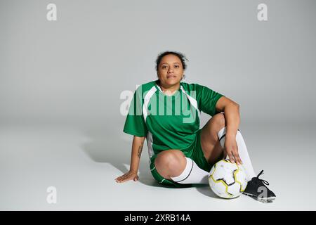 Eine Frau in einem grünen Fußballtrikot sitzt mit einem Fußball vor einem weißen Hintergrund. Stockfoto