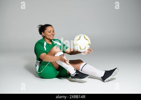 Eine Frau in einem grünen Trikot sitzt auf dem Boden und balanciert einen Fußball auf ihrem Bein. Stockfoto