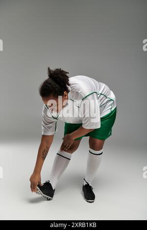 Frau in weißem Jersey und grünen Shorts wärmt sich für das Fußballspiel auf und dehnt das Bein im Studio. Stockfoto