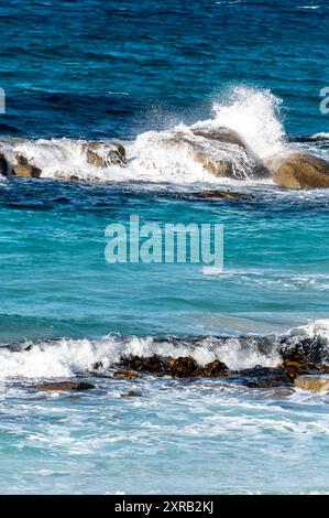 Kleine Wellen treffen auf die kleinen Felsen im Pazifischen Ozean, die an einem warmen Herbstmorgen in der Bay of Fires, ein paar Meilen, blaue und türkisfarbene Farben vermischen Stockfoto