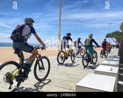 29. Juli 2024, Spanien, Platja D'Aro: Eine Gruppe von Radfahrern fährt entlang der Strandpromenade. Strände verschwinden auf der ganzen Welt. In Spanien ist das Phänomen jedoch besonders akut. Die Zeitung "La Vanguardia" schrieb kürzlich, dass der heutige Platja Gran, der "große Strand", im Durchschnitt gut 50 Meter breit und in den 1980er Jahren dreimal so groß ist Umweltschützer gehen an die Barrikaden, und die ersten Küstenstädte ergreifen drastische Maßnahmen. Foto: Emilio Rappold/dpa Stockfoto