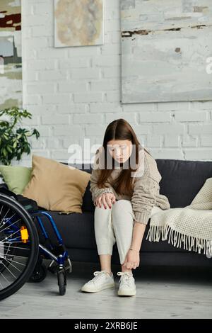 Eine junge Frau im Rollstuhl zieht ihre Schuhe an, während sie zu Hause auf einer Couch sitzt. Stockfoto