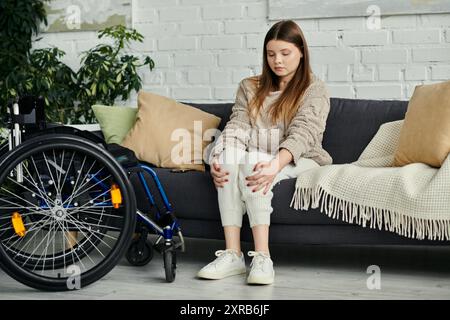 Eine junge Frau im Rollstuhl sitzt zu Hause auf einer Couch, ruht sich aus und sieht nachdenklich aus. Stockfoto