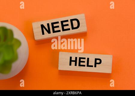 Holzblöcke beschreiben „NEED HELP“ auf einem leuchtenden orangefarbenen Hintergrund, perfekt für psychische Gesundheit oder unterstützende Themen. Stockfoto