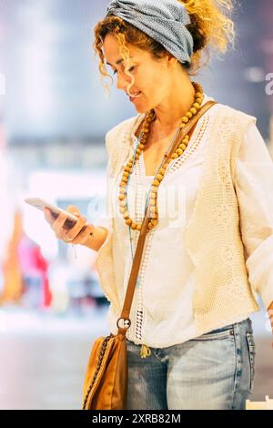 Die Leute benutzen Handys im Handelszentrum - fröhliche, hübsche Erwachsene Frau, die während des Einkaufens auf dem Smartphone schreibt - moderne trendige Kleidung für Frauen und Verbindungstechnologie Stockfoto