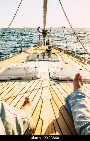 Pov Sicht der Mann Beine liegen und entspannen auf dem hölzernen Segelschiff Deck allein mit Sonnenuntergang im Hintergrund - Konzept der Reise Menschen und Freiheit im Sommerurlaub Stockfoto