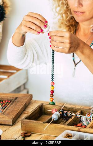 Frau zu Hause machen handgemachten Schmuck. Box mit Perlen auf alten Holztisch. Ansicht mit Frau Hände - Tutorial zu lernen, wie man Armbänder und Schmuck online und alternative Hausjob zu machen Stockfoto