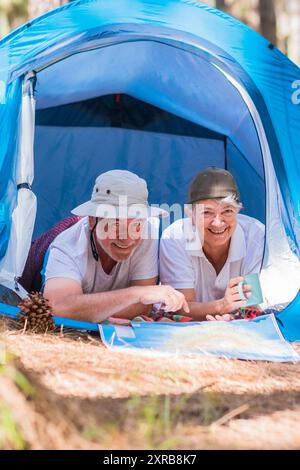 Ein paar aktive Seniorinnen und Senioren genießen gemeinsam in einem Zelt im freien Camping im Wald - junge Rentner und ein kostenloses alternatives Lifestyle-Konzept mit Liebe zur Natur - das Reisevergnügen in jedem Alter Stockfoto