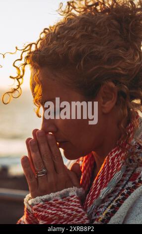 Meditation und innere Balance inneres Glückskonzept mit Seitenportrait einer jungen Frau, die im Freien betet und meditiert, mit Sonnenuntergang im Ozean im Hintergrund. Konzept der psychischen Gesundheit Lebensstil Stockfoto