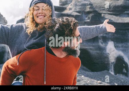 Überglücklich und kostenlos erwachsenes Paar, Mann und Frau, genießen die malerische Lage im Freien. Mann, der eine Frau mit ausgestreckten Armen und einem großen Lächeln im Gesicht trägt. Reisende, die gemeinsam Freizeitaktivitäten machen, haben Spaß Stockfoto