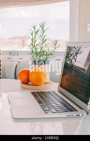 Innenansicht eines modernen Wohnmobils mit elegantem, weißem Tisch und Laptop. Das Konzept des Urlaubs und des Wohnsitzes, um das Leben eines Transporters außerhalb des Stromnetzes zu leben. Arbeitsplatz ungewöhnliches Büro- und Freiheitskonzept Stockfoto