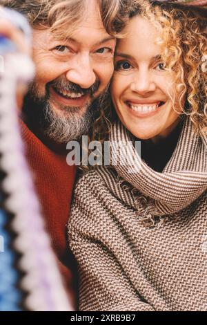 Porträt eines jungen, reifen Paares, das lächelt und gemeinsam unter einem bunten Strickmantel aus Wolle die Freizeit genießt. Liebe und Freundschaft zwischen Mann und Frau. Menschen, die Spaß haben und lachen. Urlaub Stockfoto