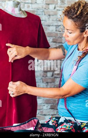 Kreative Schneiderin nimmt Größe und Maße wie ein rotes Vintage-Kleid. Das Konzept weiblicher Menschen, die im Heimstudio arbeiten und Kleider herstellen. Erwachsene Dame und Freizeitkonzept Stockfoto