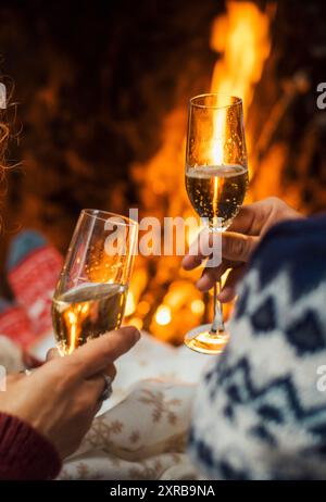 Rückansicht eines Paares, das zusammen mit Sektflöten im Haus mit Kamin im Hintergrund genießt und feiert. Winterferien und Liebe in Beziehung. Jubiläum Silvester Stockfoto