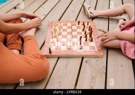 Bild von zwei Personen, die an einem Schachspiel auf einem Holzdeck beteiligt sind. Konzentrieren Sie sich auf das Schachbrett und seine durchdachten Bewegungen. Stockfoto