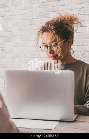 Eine Geschäftsfrau, die an der Rezeption vor einem von hinten betrachteten Mann an einem Laptop arbeitet. Konzept der Geschäftsfrau und des Kunden. Menschen arbeiten im Team zusammen. Stockfoto