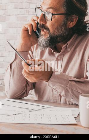 Professioneller Mitarbeiter, der am Telefon am Schreibtisch sitzt. Geschäftsmann im Gespräch auf dem Mobiltelefon. Papiernotizen und Job. Professionelle Person kommuniziert mit Stimme. Geschäftsmänner Stockfoto