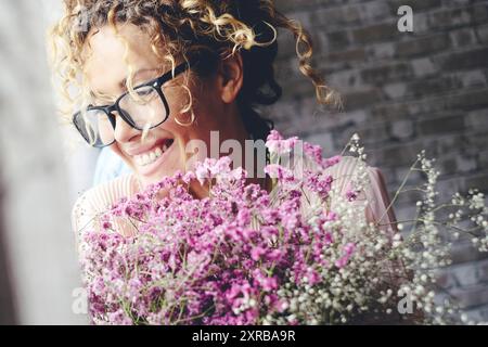 Eine aufgeregte, überfröhliche junge Frau zu Hause mit großen Blumenstraußen. Jubiläum- und Geburtstagsglücksfeier weibliche Menschen. Liebe und Beziehung. Ein neuer Freund, der zu Hause ein Geschenk bekommt Stockfoto