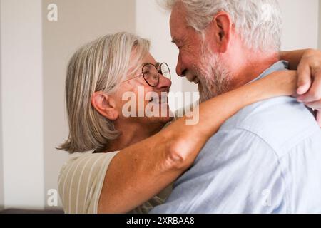 Ältere Menschen lieben das kaukasische reife Paar, das sich umarmt und sich auf die Augen sieht, lächelt und liebevoll in Beziehung steht. Seniorinnen und Senioren verbinden sich und genießen Freizeitaktivitäten im Innenbereich mit Romantik Stockfoto