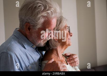 Ein älterer Mann umarmt die ältere Dame von hinten, um sie zu lieben und zu beschützen. Alter Lebensstil Leben zusammen Menschen. Ein pensioniertes Paar zu Hause denkt. Romantische sene mit Mann und Frau, die sich gegenseitig kümmern Stockfoto