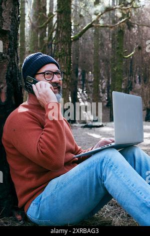 Ein Mann, der Technologie-Verbindung in Waldwäldern des Naturparks nutzt. Mitarbeiter im Außendienst, Kleinreisende, Geschäftsleute, die sich im Alltag befinden. Arbeiten im Natur-Alternativbüro. Kleine Unternehmen. Berufsleben von Reisenden Stockfoto