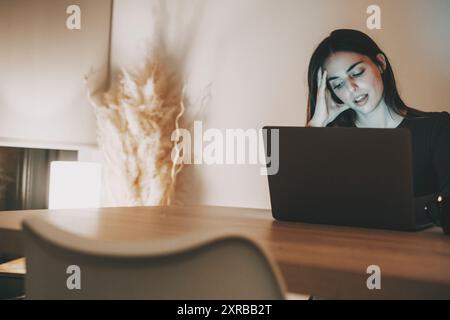 Müde Geschäftsfrau, die bis in die Nacht am Computer arbeitet. Porträt einer gestressten, zwanglosen Frau mit Kopfschmerzen am Schreibtisch. Erschöpfte Geschäftsfrau, die spät in der Nacht im Büro oder zu Hause auf einem Laptop arbeitet. Stockfoto