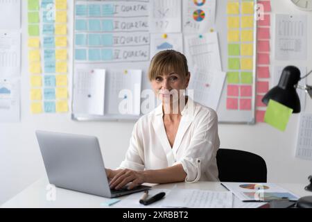 Attraktive Geschäftsfrau im Alter, leitende Geschäftsführerin, die im Büro arbeitet und vor die Kamera blickt Stockfoto