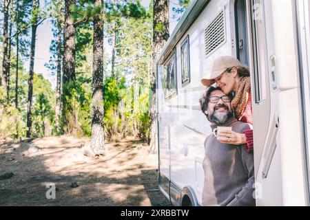 Glückliche Menschen im Reisestil sitzen vor der Tür eines Wohnmobils, der im Naturwaldpark parkt. Genießen Sie Vanlife-Paar. Mietfahrzeug für Urlaub und abseits des Stromnetzes unabhängiges Haus Wohnmobil Stockfoto