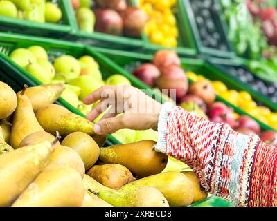 Nahaufnahme weibliche Hände, die Obst auf dem Markt nehmen, schöne, hübsche junge Frau im Pullover, die grünes Blattgemüse im Supermarkt auswählt Stockfoto