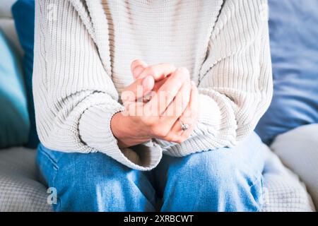 Vorderansicht einer depressiven, traurigen, Reifen Frau zu Hause, die allein auf dem Sofa sitzt und mit gefalteten Händen nach unten blickt. Nachdenkliche weibliche Menschen und Einsamkeit Stockfoto