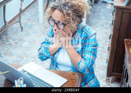 Überraschte und aufgeregte Frau vor einem Laptop, die Hände am Mund hält und mit unglaublichem Ausdruck auf den Bildschirm schauen. Gewinner Online-Lotterie oder erfolgreicher E-Mail-Job erhalten. Großes Überraschungs-Notebook Stockfoto