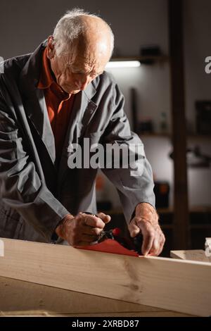 Zimmermann im Alter. Holzbearbeitung auf rohem Holz mit einer Hobelmaschine Stockfoto