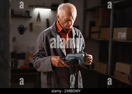 Ein alter Zimmermann hält eine Schleifmaschine, um Schleifpapier zu ersetzen, während er abends Überstunden in seiner Werkstatt macht Stockfoto