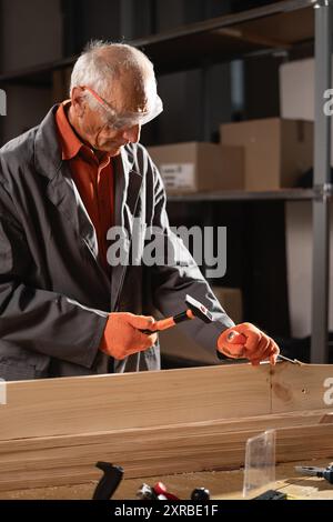 Senior Zimmermann formt Holz mit Meißel und Hammer Stockfoto