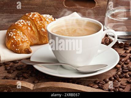 Kaffee mit Croissant und Glas Wasser in der Schale aus braunem Holz. Stockfoto