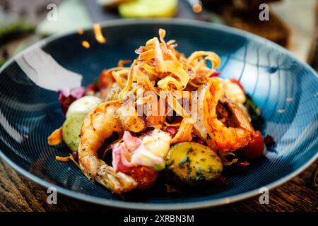 Warmer Salat mit argentinischen Königsgarnelen. Mandelkartoffel, Mini-Romana-Salat, Karotten, Kirschtomaten, Pesto, Schwarze Wurzelchips, karamellisierte Walnüsse, Rüben Stockfoto