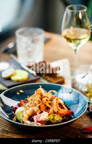 Warmer Salat mit argentinischen Königsgarnelen. Mandelkartoffel, Mini-Romana-Salat, Karotten, Kirschtomaten, Pesto, Schwarze Wurzelchips, karamellisierte Walnüsse, Rüben Stockfoto