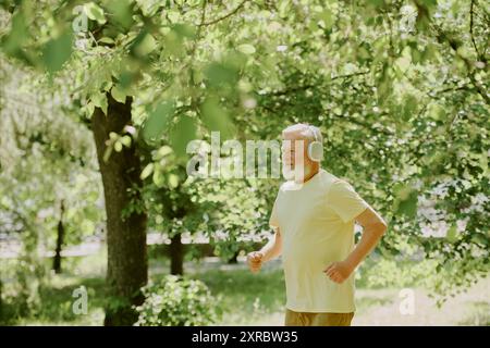 Silberhaariger Rentner, der im Park läuft und Musik und die Natur des Sommers genießt Stockfoto