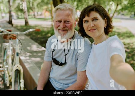 Ältere Brünette, die Selfie mit ihrem geliebten silberhaarigen Ehemann macht, während sie laufen Stockfoto