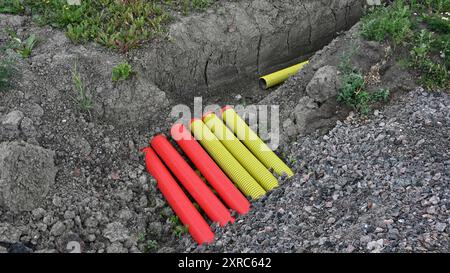 Das Bild zeigt eine Baustelle mit einem Graben mit leuchtend roten und gelben Rohren, die wahrscheinlich für Versorgungsleitungen oder Kabelinstallationen geeignet sind Stockfoto