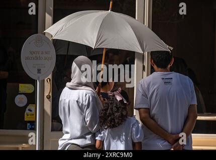 Barcelona, Spanien. August 2024. Eine Familie, die sich mit einem Sonnenschirm vor der Sonne schützte, während sie darauf wartete, in einem Café im Zentrum von Barcelona serviert zu werden. Barcelona leidet wieder einmal unter einer Hitzewelle mit Temperaturen von 40 Grad auf dem Asphalt des Stadtzentrums. Quelle: SOPA Images Limited/Alamy Live News Stockfoto