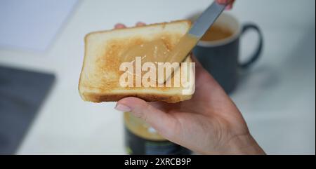 Schmiert Erdnussbutter von Hand auf knusprigem Toast, Nahaufnahme Stockfoto