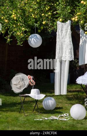 Festliche weiße Kleider für Frauen und Kinder hängen an einem Apfelbaum im Garten, wählen ein Hochzeitskleid, bereiten sich auf die Hochzeit vor Stockfoto