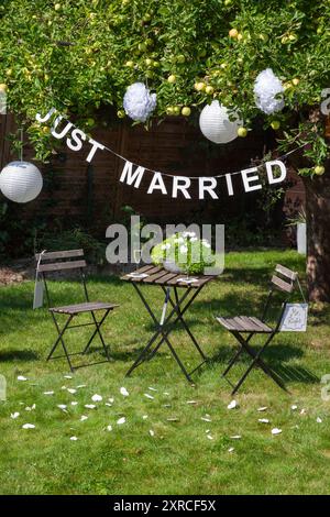 Eine Girlande mit der Inschrift "Just Married" hängt an einem Apfelbaum mit grünen Äpfeln und weißen Laternen im Garten, ein Schild mit der Inschrift Mr.. Stockfoto