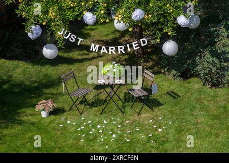 Eine Girlande mit der Inschrift Just Married hängt an einem Apfelbaum mit grünen Äpfeln und weißen Laternen im Garten, ein Schild mit der Inschrift Mr. Right hängt an einem Stuhl, Vorbereitungen und Dekoration für eine Hochzeit im Garten, Berlin, Deutschland Stockfoto