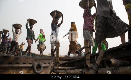 Eine menschliche Kette von Trägern trägt Kohle, Sand und Kies von den Bargen, die an der Aminbazar Landing Station am Buriganga River außerhalb von Dhaka festgemacht sind. Bangladesch absolviert derzeit den Abschluss der LDC-Kategorie (am wenigsten entwickelte Länder), was zum großen Teil der extrem harten Arbeit billiger Arbeitskräfte zu verdanken ist. Ein Portier macht zwischen 80 und 140 USD pro Monat, laut den Websites paylab.com und averagesalarysurvey.com Stockfoto