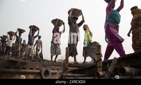 Eine menschliche Kette von Trägern trägt Kohle, Sand und Kies von den Bargen, die an der Aminbazar Landing Station am Buriganga River außerhalb von Dhaka festgemacht sind. Bangladesch absolviert derzeit den Abschluss der LDC-Kategorie (am wenigsten entwickelte Länder), was zum großen Teil der extrem harten Arbeit billiger Arbeitskräfte zu verdanken ist. Ein Portier macht zwischen 80 und 140 USD pro Monat, laut den Websites paylab.com und averagesalarysurvey.com Stockfoto