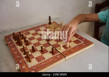 Ein Nahaufnahme-Foto, das eine Hand zeigt, die ein Schachstück auf einem hölzernen Schachbrett bewegt und die Strategie und Konzentration des Spiels unterstreicht. Stockfoto